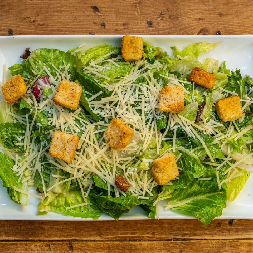 Caesar salad with crisp romaine lettuce, shredded Parmesan cheese, and golden croutons on a white plate.