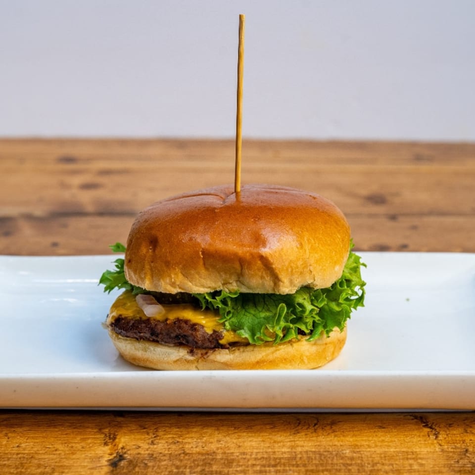 A cheeseburger with lettuce and onions on a white plate, held together by a toothpick.