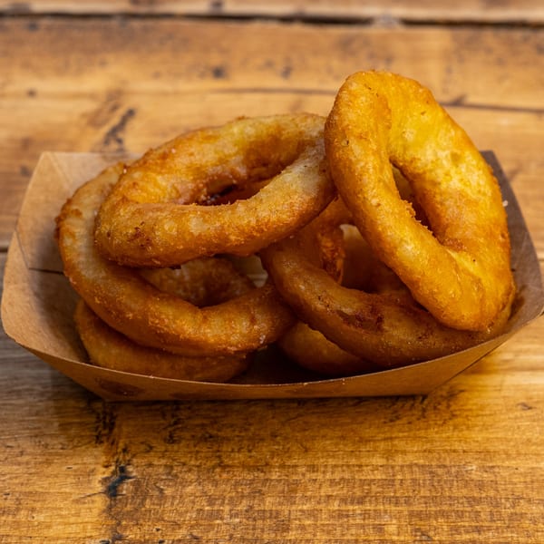 Golden-brown onion rings from Burger U, served in a paper tray on a rustic wooden table.