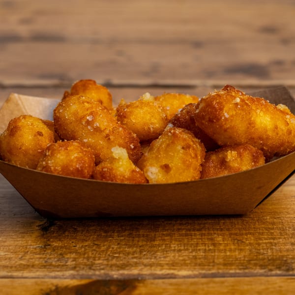 Golden-brown, crispy fried cheese curds with salt crystals in a brown paper tray on a wooden table.