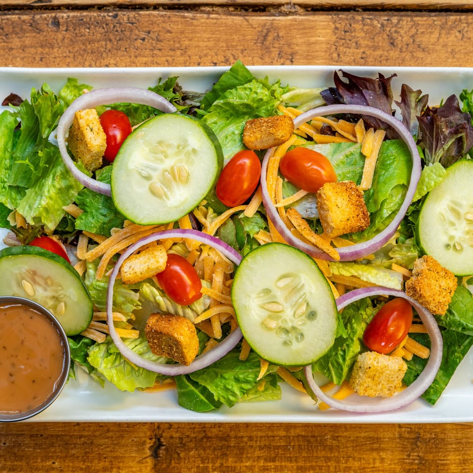 A fresh side salad with mixed greens, cherry tomatoes, cucumbers, red onion, shredded cheese, and croutons.