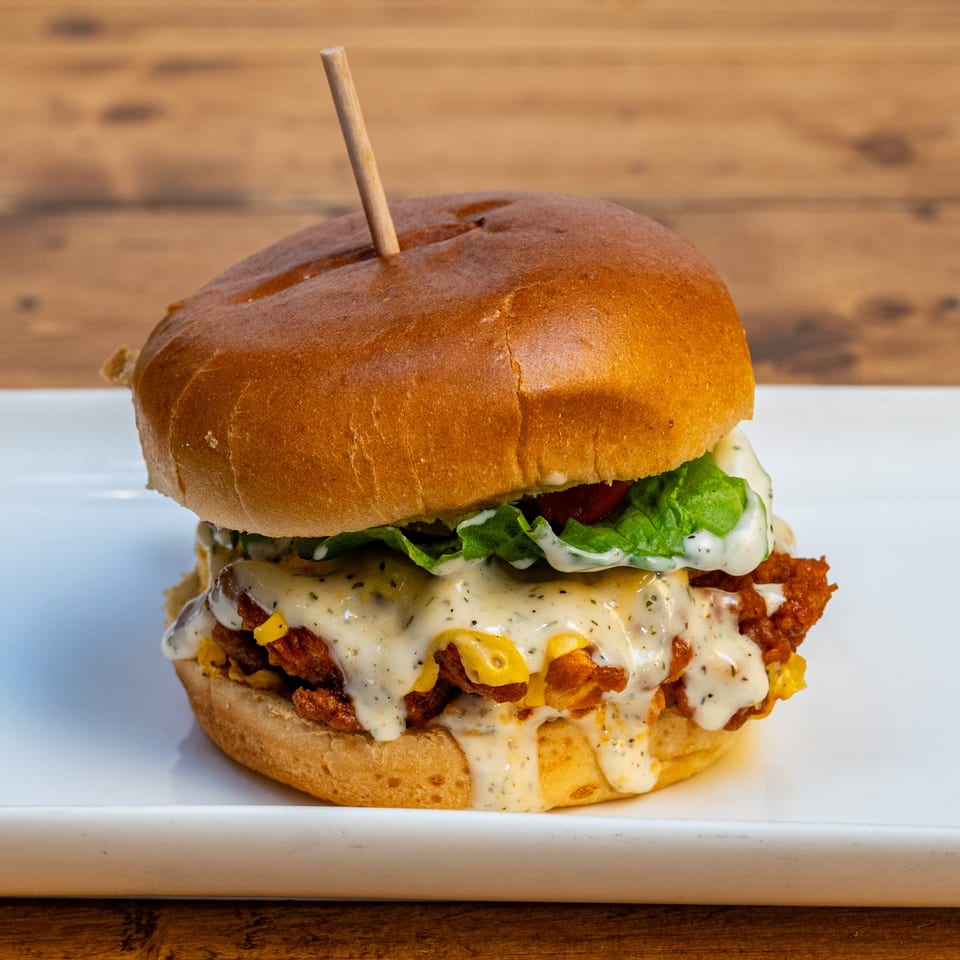 A Burger U chicken sandwich with melted cheese, lettuce, and creamy sauce on a white plate.