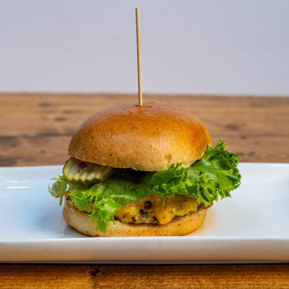 A cheeseburger with lettuce and pickles on a white plate, held together by a toothpick.