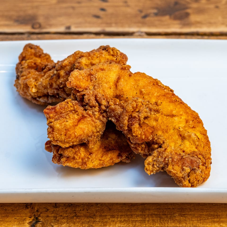 Crispy, golden-brown chicken tenders from Burger U, served on a white rectangular plate.