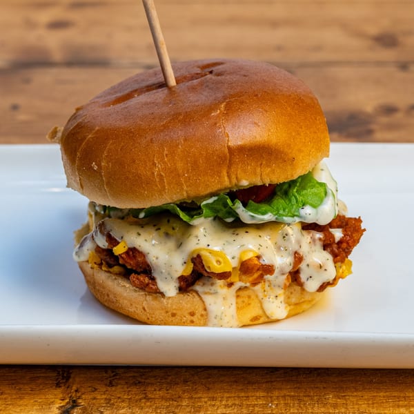 A Burger U fried chicken sandwich with melted cheese, lettuce, and creamy sauce on a white plate.