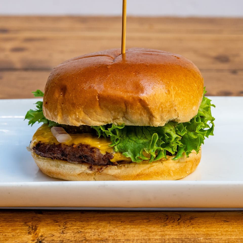A Burger U cheeseburger with lettuce and onions on a white plate, against a wooden background.