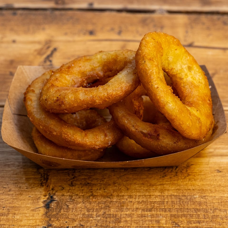 Golden-brown onion rings in a cardboard tray on a rustic wooden table at Burger U.
