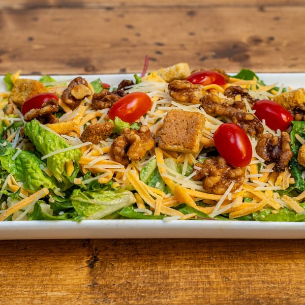 A fresh Burger U salad with green lettuce, shredded cheese, walnuts, croutons, and cherry tomatoes.
