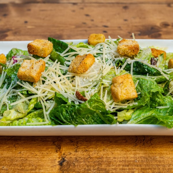A Caesar salad with romaine lettuce, croutons, and shredded Parmesan cheese on a white plate.