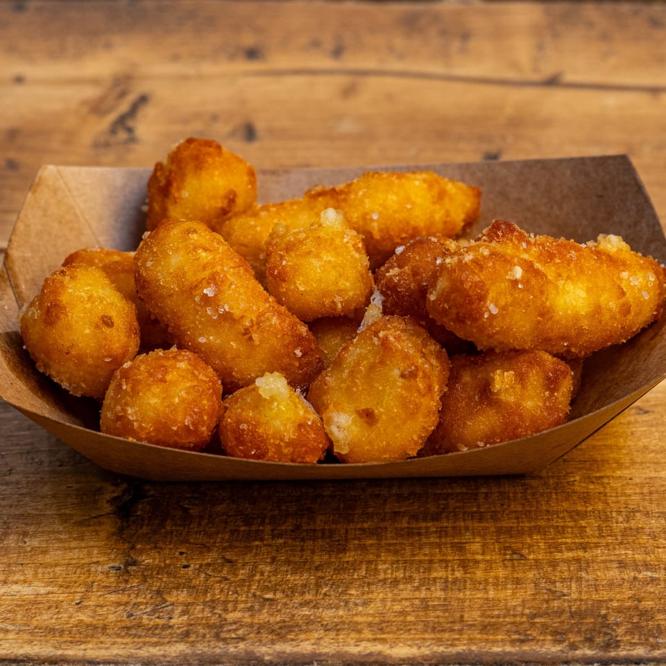 Golden brown fried cheese curds with visible salt crystals in a paper tray on a wooden surface.
