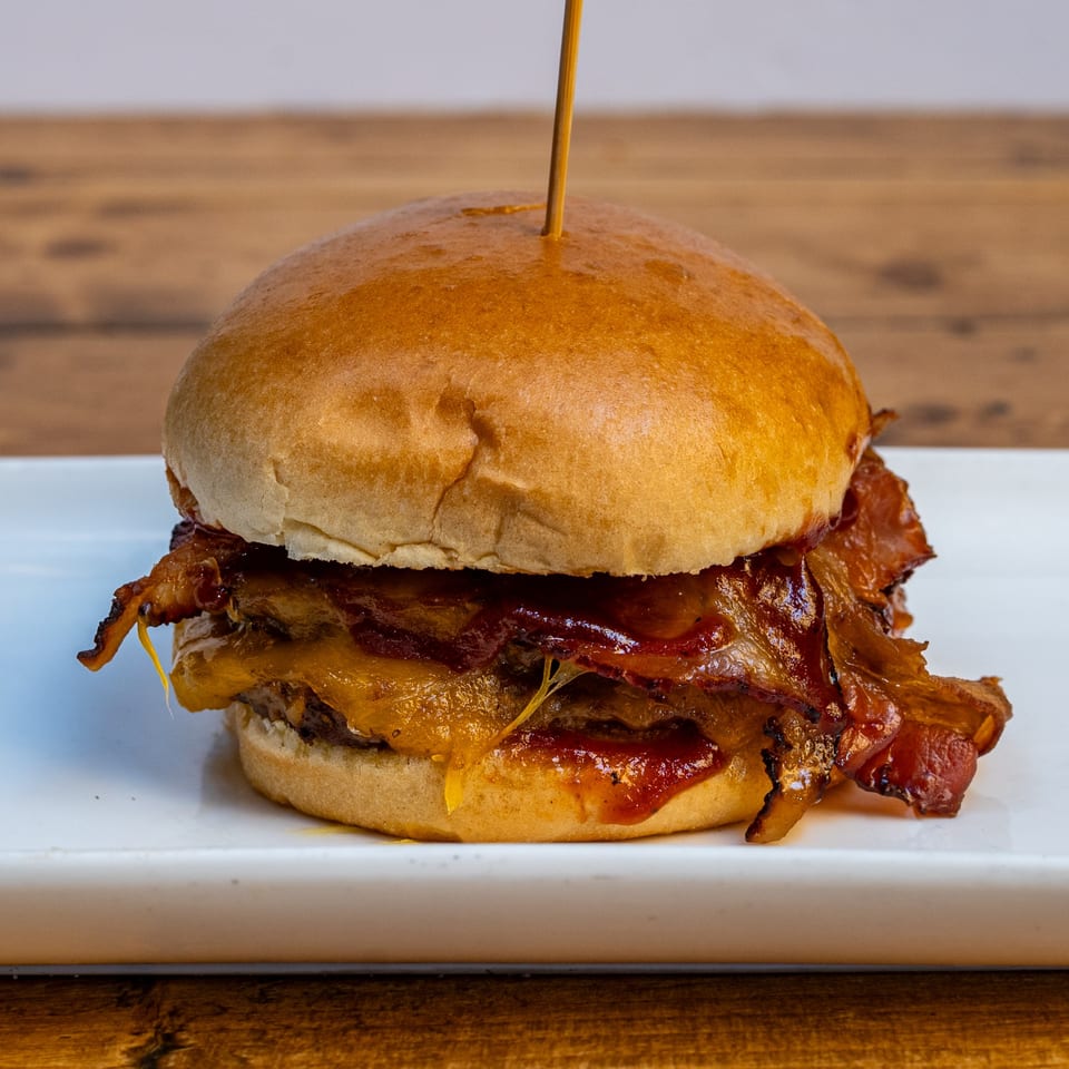 A Burger U burger with melted cheese, crispy bacon, and barbecue sauce on a white plate.